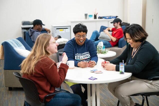 A group of people socialize around a table, with others in the background