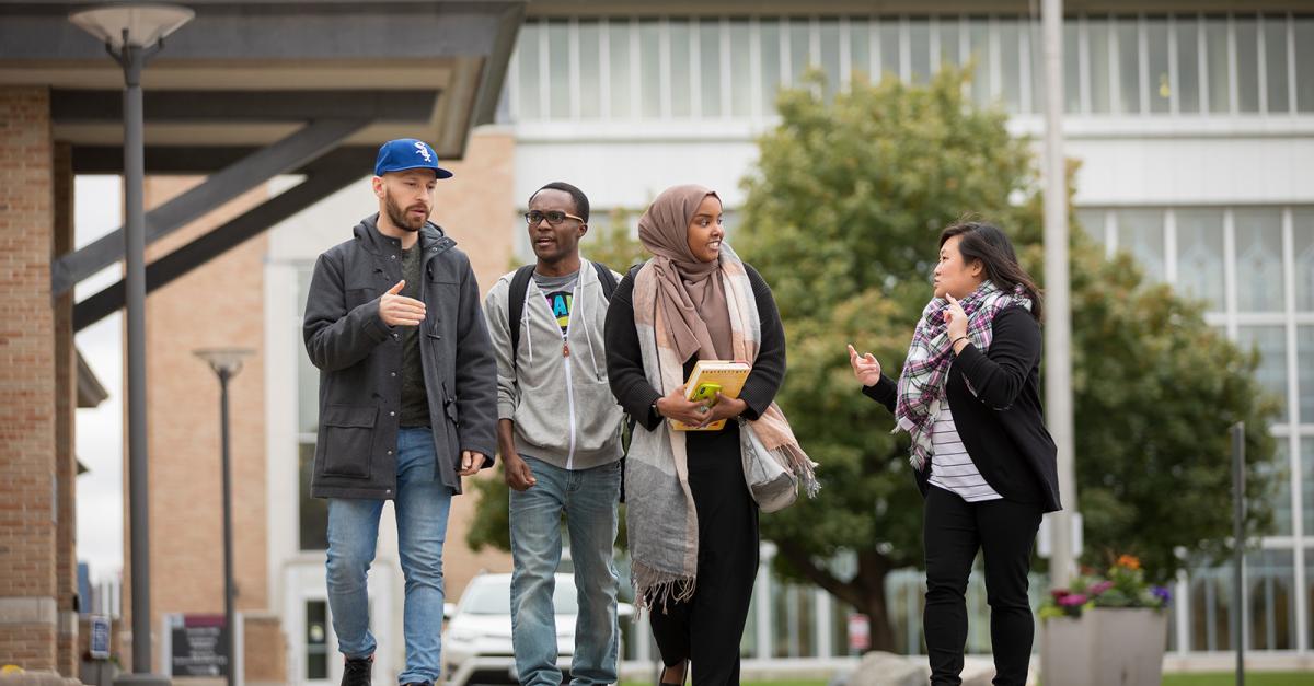 Four young adults walk on a college campus on an early fall day