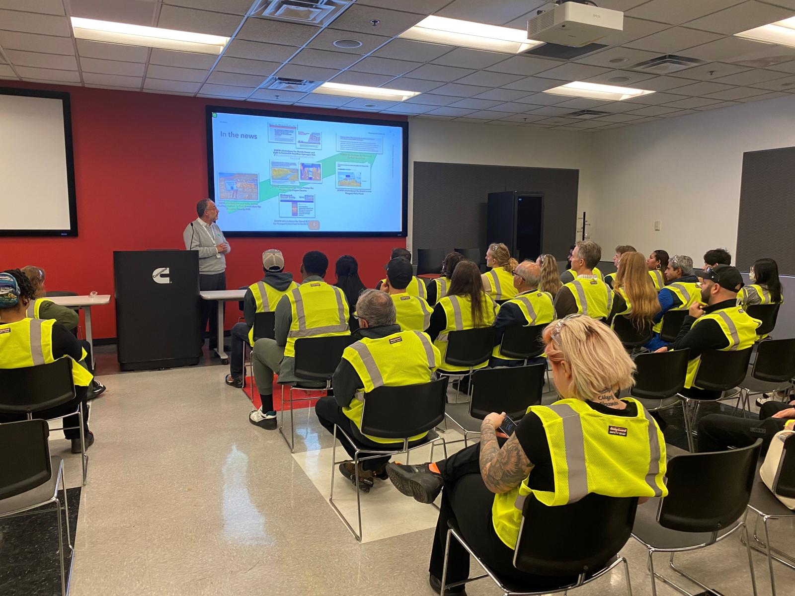 A group of people in yellow high visibility vests sit for a classroom presentation