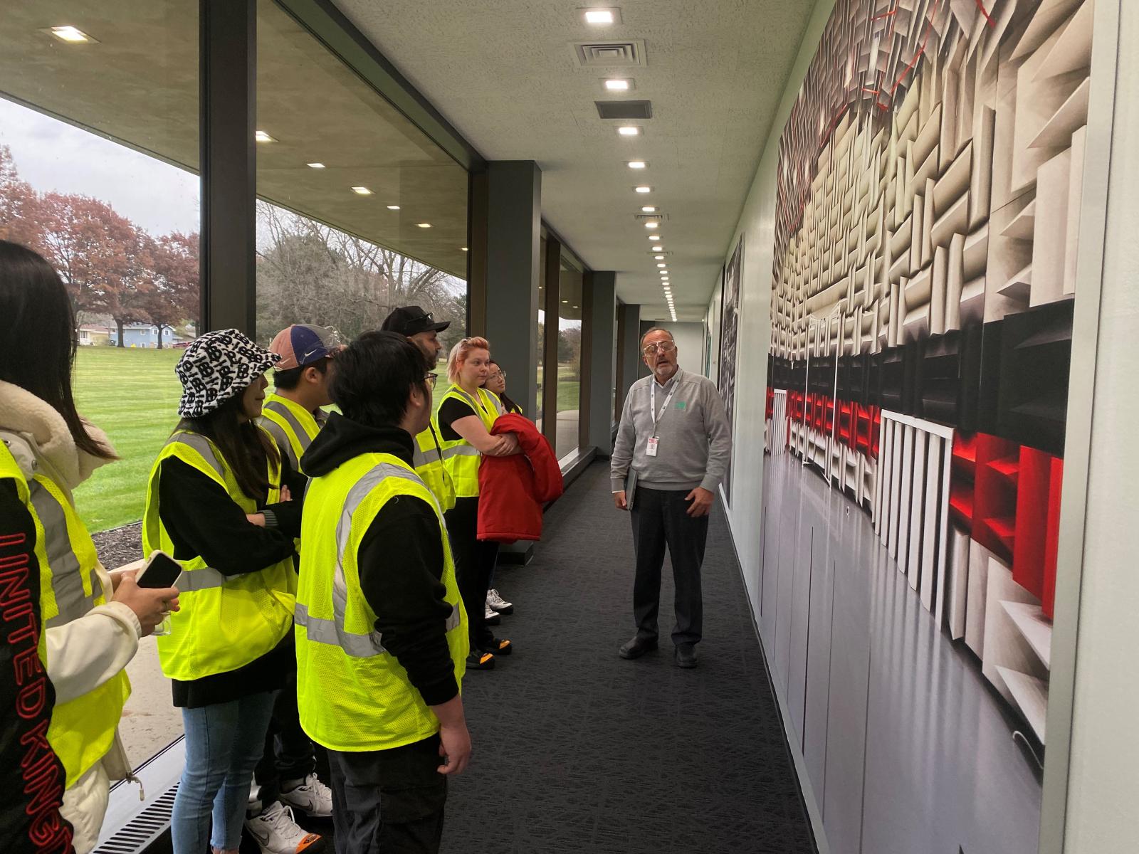 A person guiding a tour group of people wearing high visibility vests in a hallway