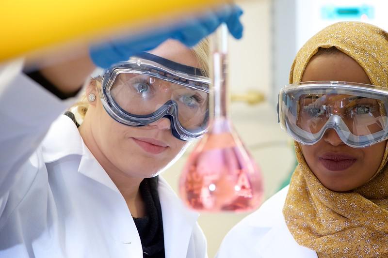 Two students in lab gear observe a beaker