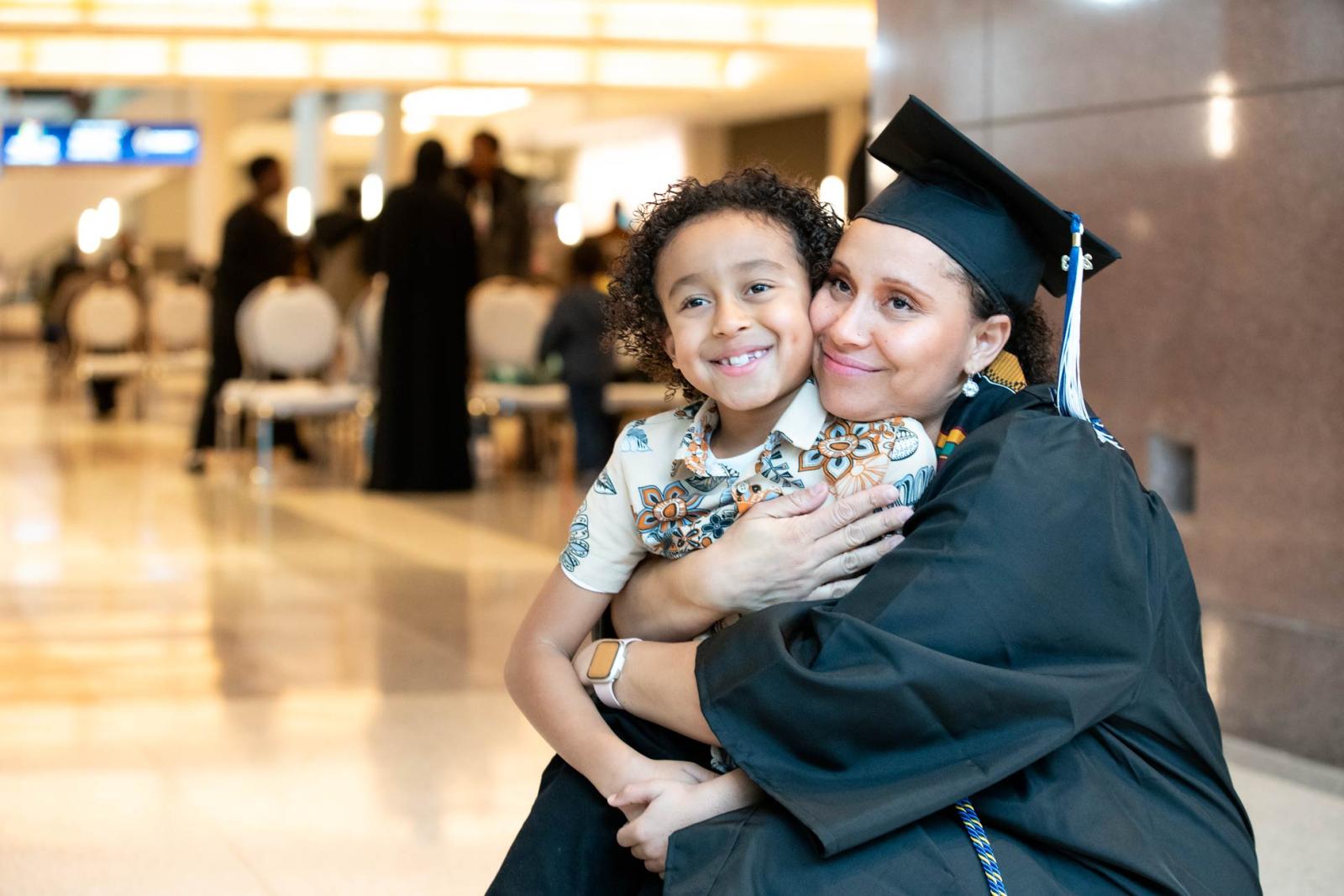 A woman in cap and gown hugs a child