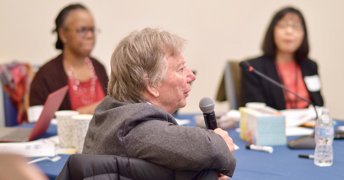 Dr. Craig Hansen, holding a microphone as he speaks from a workgroup table at a fundraising event