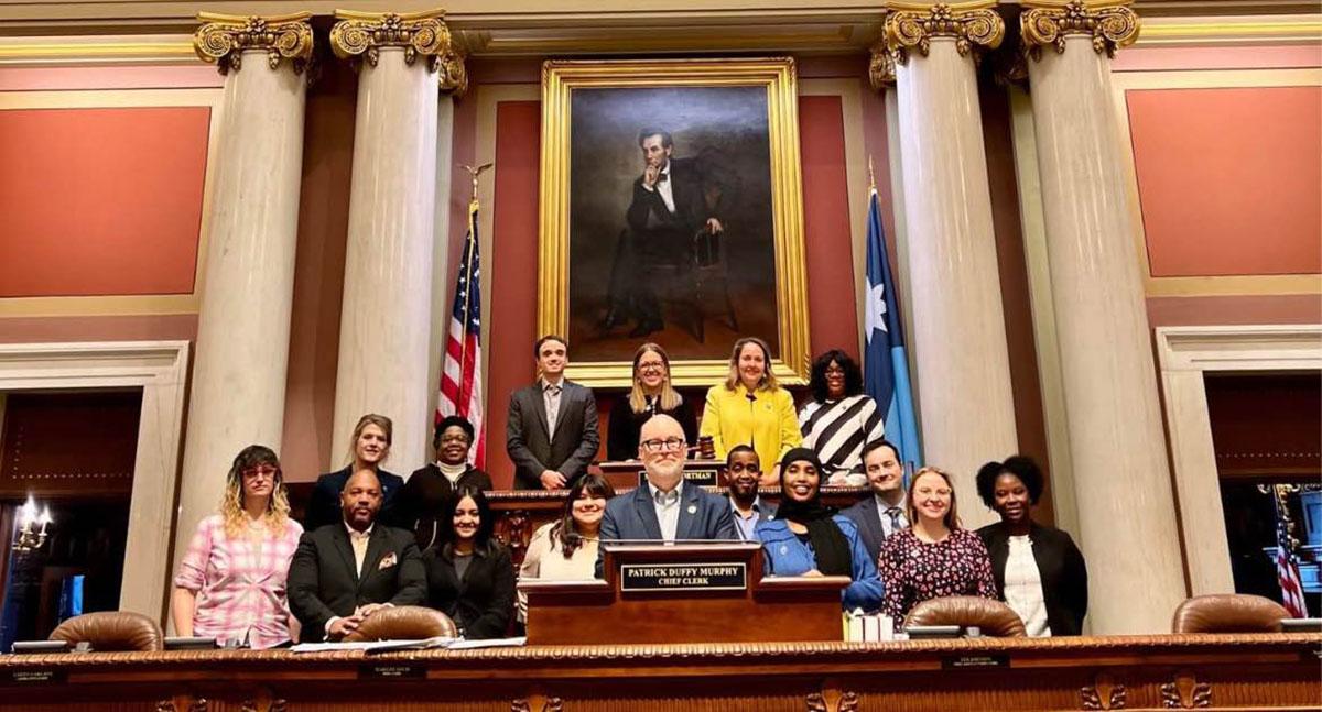 A group of people pose for a photo behind the lectern in the Minnesota State Capitol