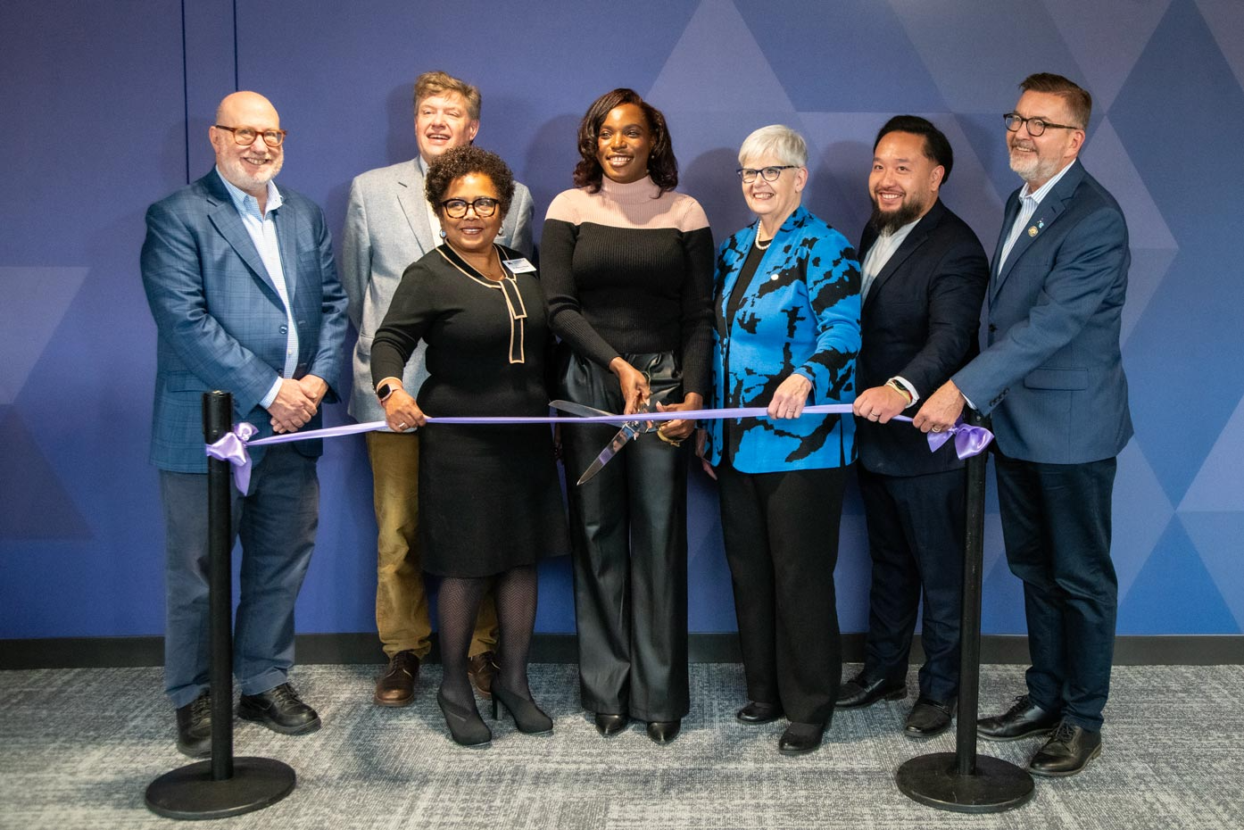 A group of people pose while preparing to cut a ceremonial ribbon