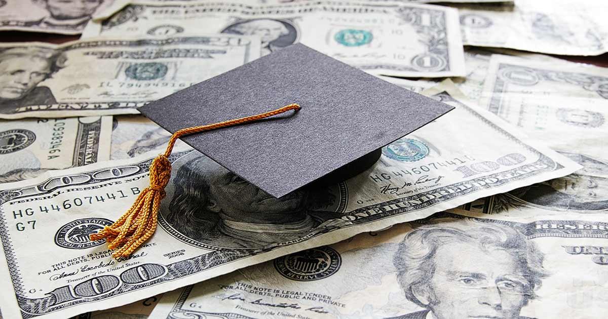 A graduation cap rests on a pile of U.S. currency.