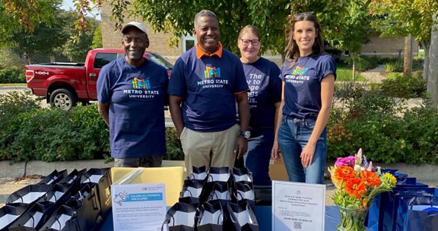 A group of volunteers pose behind a table of giveaways at Metro State's 2024 Fall Fest